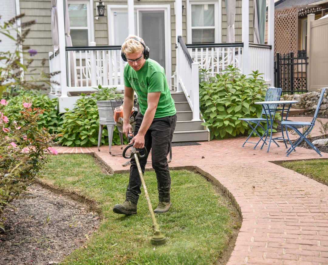 Home Man weed wacking a customers grass next to a sidewalk with the house in the background.